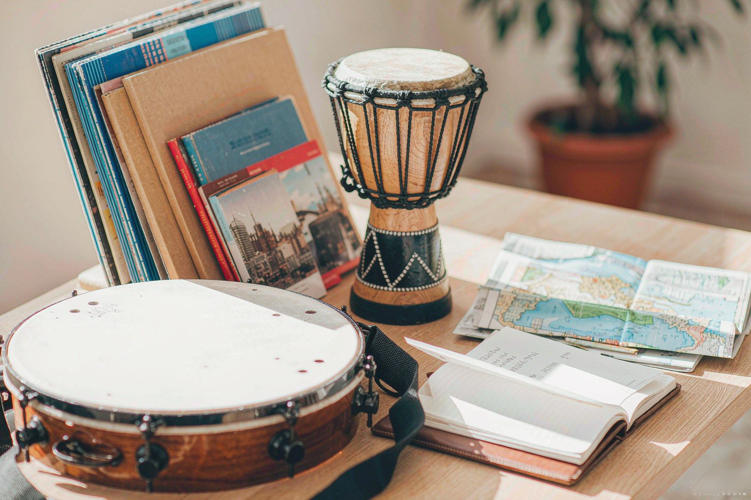 A pandeiro and a djembe on a songwriter’s desk with postcards, a folded map and an open notebook in afternoon light